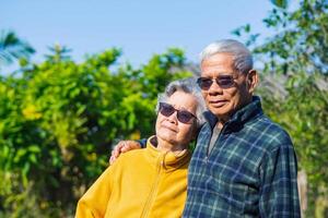 ritratto di un' romantico anziano asiatico coppia sorridente e guardare a il telecamera mentre in piedi nel un' giardino. anziano coppia. concetto di anziano persone e assistenza sanitaria foto