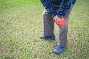 un anziano asiatico uomo sofferenza a partire dal un' ginocchio dolore mentre in piedi nel un' giardino. spazio per testo. concetto di anziano persone e assistenza sanitaria foto