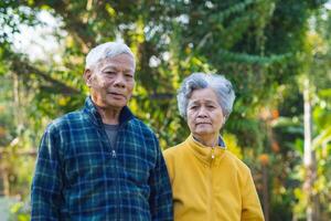 anziano coppia sorridente e guardare a il telecamera mentre in piedi nel un' giardino. concetto di anziano persone e assistenza sanitaria foto