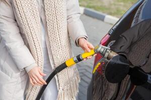 giovane donna Tenere un' carburante ugello nel sua mano mentre rifornimento carburante auto a gas stazione. un' fermare per rifornimento carburante a il gas stazione. fare il pieno il auto con gas. foto