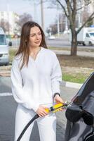 giovane donna Tenere un' carburante ugello nel sua mano mentre rifornimento carburante auto a gas stazione. un' fermare per rifornimento carburante a il gas stazione. fare il pieno il auto con gas. foto