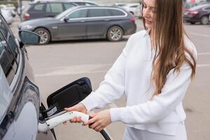 giovane donna ricarica sua elettrico auto a un' ricarica stazione nel il città. eco carburante concetto. il concetto di l'ambiente amichevole trasporto. ricarica batteria a partire dal ricarica stazione. foto