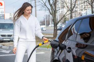 giovane donna Tenere un' carburante ugello nel sua mano mentre rifornimento carburante auto a gas stazione. un' fermare per rifornimento carburante a il gas stazione. fare il pieno il auto con gas. foto