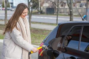 giovane donna Tenere un' carburante ugello nel sua mano mentre rifornimento carburante auto a gas stazione. un' fermare per rifornimento carburante a il gas stazione. fare il pieno il auto con gas. foto