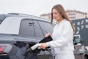 giovane donna ricarica sua elettrico auto a un' ricarica stazione nel il città. eco carburante concetto. il concetto di l'ambiente amichevole trasporto. ricarica batteria a partire dal ricarica stazione. foto