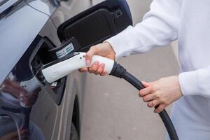 giovane donna ricarica sua elettrico auto a un' ricarica stazione nel il città. eco carburante concetto. il concetto di l'ambiente amichevole trasporto. ricarica batteria a partire dal ricarica stazione. foto