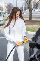 giovane donna Tenere un' carburante ugello nel sua mano mentre rifornimento carburante auto a gas stazione. un' fermare per rifornimento carburante a il gas stazione. fare il pieno il auto con gas. foto