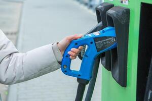 giovane attività commerciale donna rifornimento carburante sua elettrico auto a un' ev ricarica stazione. concetto di l'ambiente amichevole veicolo. elettrico auto concetto. verde in viaggio. foto