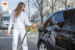 giovane donna Tenere un' carburante ugello nel sua mano mentre rifornimento carburante auto a gas stazione. un' fermare per rifornimento carburante a il gas stazione. fare il pieno il auto con gas. foto