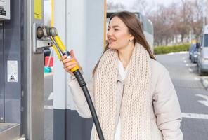 giovane donna Tenere un' carburante ugello nel sua mano mentre rifornimento carburante auto a gas stazione. un' fermare per rifornimento carburante a il gas stazione. fare il pieno il auto con gas. foto