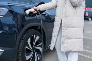 giovane donna ricarica sua elettrico auto a un' ricarica stazione nel il città. eco carburante concetto. il concetto di l'ambiente amichevole trasporto. ricarica batteria a partire dal ricarica stazione. foto