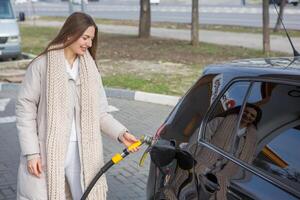 giovane donna Tenere un' carburante ugello nel sua mano mentre rifornimento carburante auto a gas stazione. un' fermare per rifornimento carburante a il gas stazione. fare il pieno il auto con gas. foto