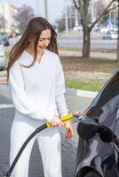 giovane donna Tenere un' carburante ugello nel sua mano mentre rifornimento carburante auto a gas stazione. un' fermare per rifornimento carburante a il gas stazione. fare il pieno il auto con gas. foto