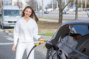 giovane donna Tenere un' carburante ugello nel sua mano mentre rifornimento carburante auto a gas stazione. un' fermare per rifornimento carburante a il gas stazione. fare il pieno il auto con gas. foto