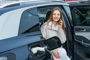 giovane attività commerciale donna rifornimento carburante sua elettrico auto a un' ev ricarica stazione. concetto di l'ambiente amichevole veicolo. elettrico auto concetto. verde in viaggio. foto