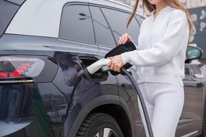 giovane donna ricarica sua elettrico auto a un' ricarica stazione nel il città. eco carburante concetto. il concetto di l'ambiente amichevole trasporto. ricarica batteria a partire dal ricarica stazione. foto