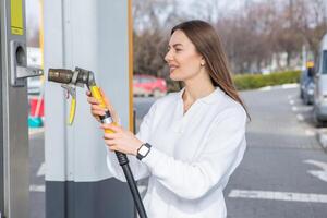 giovane donna Tenere un' carburante ugello nel sua mano mentre rifornimento carburante auto a gas stazione. un' fermare per rifornimento carburante a il gas stazione. fare il pieno il auto con gas. foto