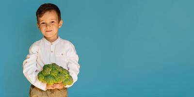 un' studio tiro di un' ragazzo Tenere fresco broccoli su un' blu sfondo con un' copia di il spazio. il concetto di salutare bambino cibo. foto
