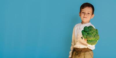 un' studio tiro di un' sorridente ragazzo Tenere fresco broccoli su un' blu sfondo con un' copia di il spazio. il concetto di salutare bambino cibo. foto