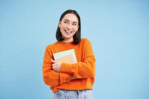 sorridente asiatico donna con i Quaderni, alunno con contento viso, promo di Università formazione scolastica, blu sfondo foto