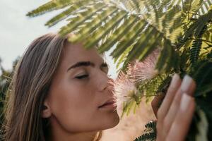 bellezza ritratto di contento donna avvicinamento. giovane ragazza odorare Cinese acacia rosa fioritura fiori. ritratto di giovane donna nel fioritura molla, estate giardino. romantico vibrazione. femmina e natura foto