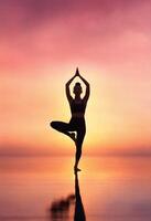 ai generato silhouette di giovane donna praticante yoga su il spiaggia a tramonto. ai generativo foto