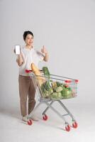 sorridente donna felicemente spingendo un' supermercato carrello, isolato su bianca sfondo foto