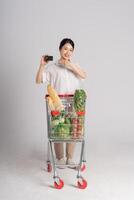 sorridente donna felicemente spingendo un' supermercato carrello, isolato su bianca sfondo foto