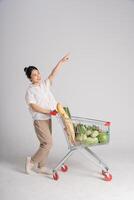 sorridente donna felicemente spingendo un' supermercato carrello, isolato su bianca sfondo foto