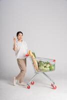 sorridente donna felicemente spingendo un' supermercato carrello, isolato su bianca sfondo foto