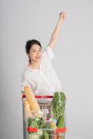 sorridente donna felicemente spingendo un' supermercato carrello, isolato su bianca sfondo foto