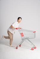 sorridente donna felicemente spingendo un' supermercato carrello, isolato su bianca sfondo foto