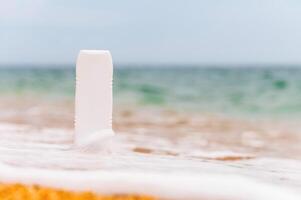 un' bottiglia di protezione solare senza un' etichetta su il spiaggia su un' soleggiato giorno. vuoto per pubblicità il tuo crema e etichette foto