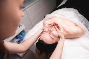 avvicinamento tiro di un' donna di testa fare un' facciale massaggio su un' trattamento tavolo. terapista l'applicazione pressione con pollici su fronte foto