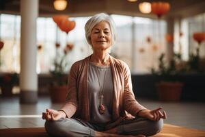 ai generato calma sorridente anziano donna praticante yoga, Meditare mentre seduta nel loto posizione nel sala foto