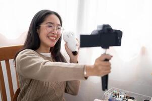 un' sorridente asiatico femmina soddisfare Creatore è parlando con il telecamera, mostrando sua fatto a mano peluche. foto