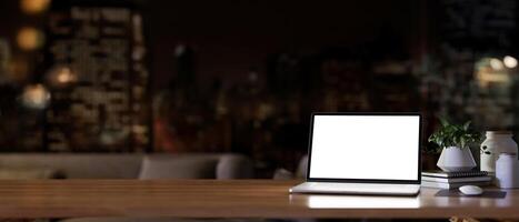 un' bianca schermo il computer portatile computer su un' di legno scrivania nel un' moderno buio vivente camera a notte. foto