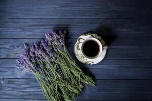 un' tazza di caffè, mazzo di lavanda e dolce su buio blu di legno tavolo. foto