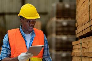 africano lavoratore falegname indossare sicurezza uniforme e difficile cappello Lavorando e controllo il qualità di di legno prodotti a laboratorio produzione. uomo e donna lavoratori legna nel buio magazzino industria. foto