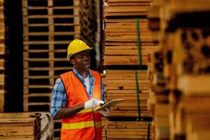 africano lavoratore falegname indossare sicurezza uniforme e difficile cappello Lavorando e controllo il qualità di di legno prodotti a laboratorio produzione. uomo e donna lavoratori legna nel buio magazzino industria. foto