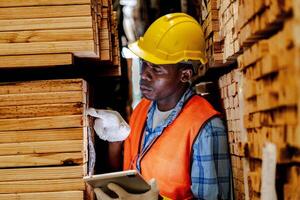 africano lavoratore falegname indossare sicurezza uniforme e difficile cappello Lavorando e controllo il qualità di di legno prodotti a laboratorio produzione. uomo e donna lavoratori legna nel buio magazzino industria. foto