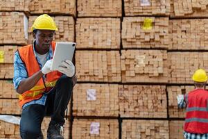 africano lavoratori uomo ingegneria a piedi e ispezionando con Lavorando suite vestito e mano guanto nel legname legna magazzino. concetto di inteligente industria lavoratore operativo. legna fabbriche produrre legna palato. foto