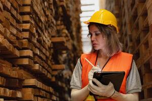 donna lavoratore falegname indossare sicurezza uniforme e difficile cappello Lavorando e controllo il qualità di di legno prodotti a laboratorio produzione. uomo e donna lavoratori legna nel buio magazzino industria. foto