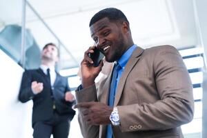 inteligente nero uomo d'affari Guardando mobile Telefono. Calvo adulto uomo indossare formale indossare. riflessivo afroamericano uomo d'affari nel un' perfettamente su misura completo da uomo in piedi nel scala nel ufficio. foto