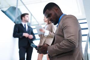 inteligente nero uomo d'affari Guardando mobile Telefono. Calvo adulto uomo indossare formale indossare. riflessivo afroamericano uomo d'affari nel un' perfettamente su misura completo da uomo in piedi nel scala nel ufficio. foto