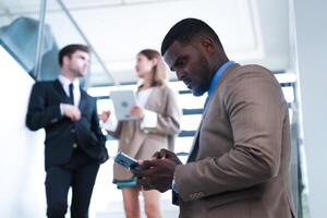 inteligente nero uomo d'affari Guardando mobile Telefono. Calvo adulto uomo indossare formale indossare. riflessivo afroamericano uomo d'affari nel un' perfettamente su misura completo da uomo in piedi nel scala nel ufficio. foto