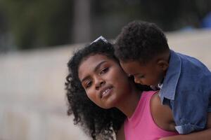 misto gara africano e asiatico madre e ragazzo è giocando a il all'aperto la zona. sorridente contento famiglia avere divertimento in esecuzione su il spiaggia. ritratto di mamma e ragazzo stile di vita con un' unico acconciatura. foto