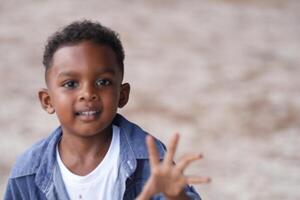 misto gara africano e asiatico ragazzo è giocando a il all'aperto la zona. sorridente contento ragazzo ha divertimento in esecuzione su il spiaggia. ritratto di ragazzo stile di vita con un' unico acconciatura. foto