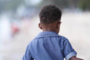 misto gara africano e asiatico ragazzo è giocando a il all'aperto la zona. sorridente contento ragazzo ha divertimento in esecuzione su il spiaggia. ritratto di ragazzo stile di vita con un' unico acconciatura. foto