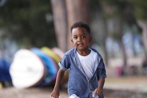 misto gara africano e asiatico ragazzo è giocando a il all'aperto la zona. sorridente contento ragazzo ha divertimento in esecuzione su il spiaggia. ritratto di ragazzo stile di vita con un' unico acconciatura. foto